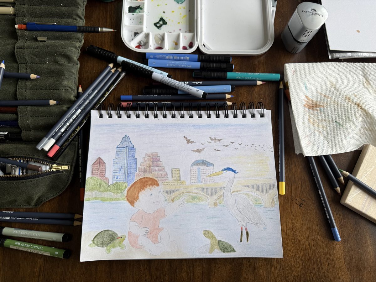 The finished Austin page on the drawing table, surrounded by colored pencils, a watercolor palette and a paint-stained paper towel.